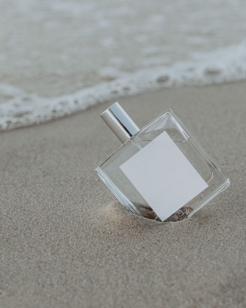 Clear perfume bottle standing on wet sand by the sea