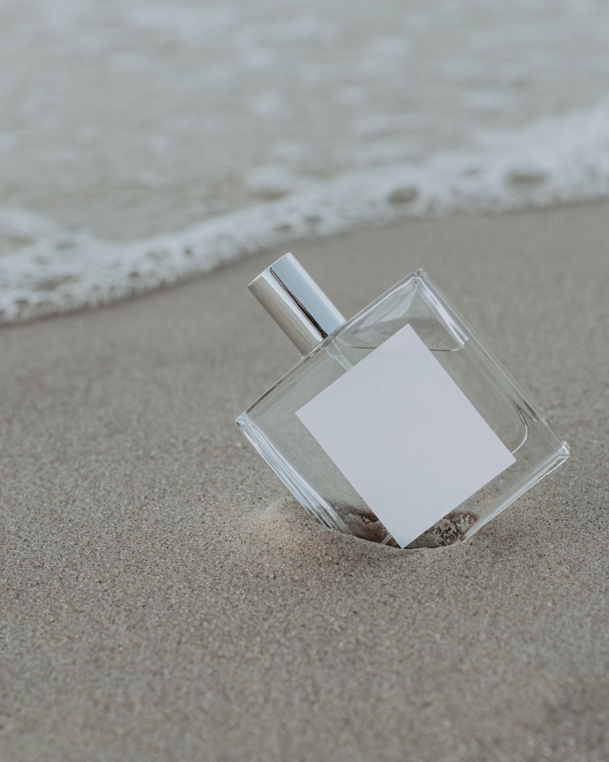 Clear perfume bottle standing on wet sand by the sea