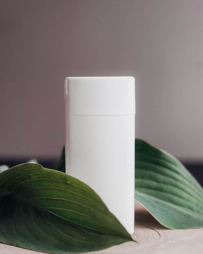 White deodorant stick beside green leaves