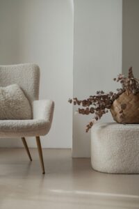 Oat boucle lounge chair on oak legs beside a pouf