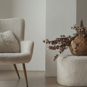 Oat boucle lounge chair on oak legs beside a pouf