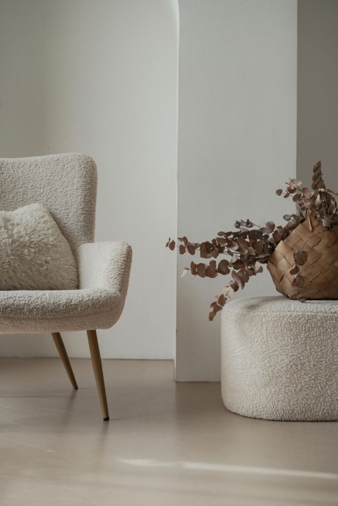 Oat boucle lounge chair on oak legs beside a pouf