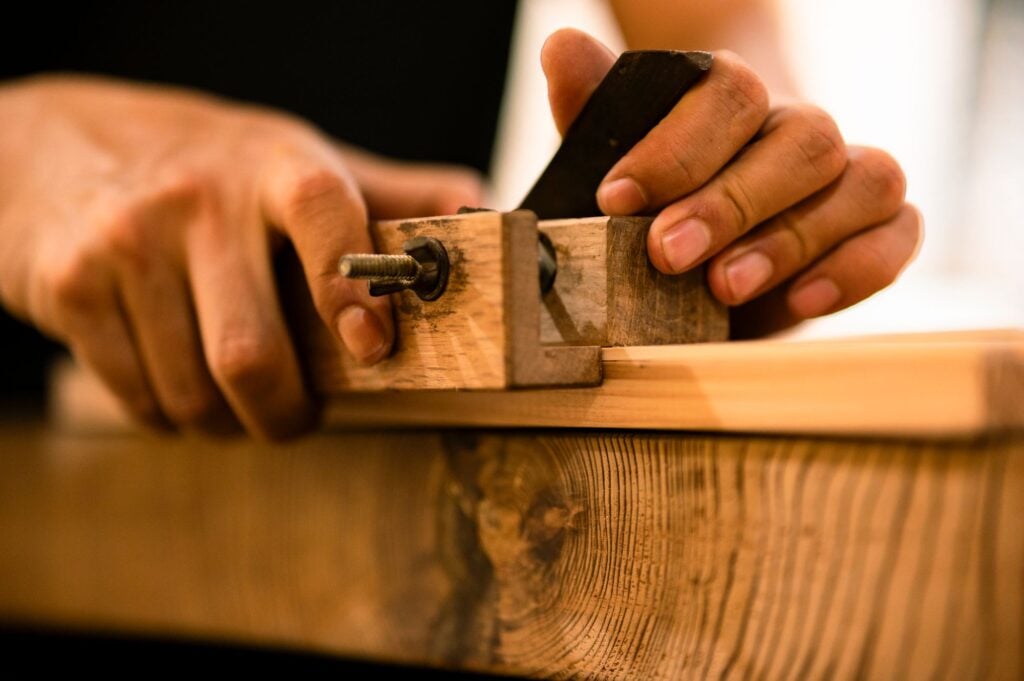 Hands guiding a hand plane over oak with curled shavings