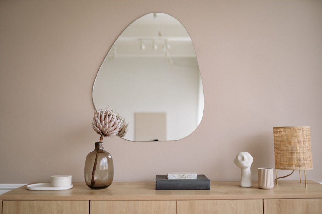 Organic-shaped mirror above a beige sideboard with ceramics