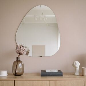 Organic-shaped mirror above a beige sideboard with ceramics