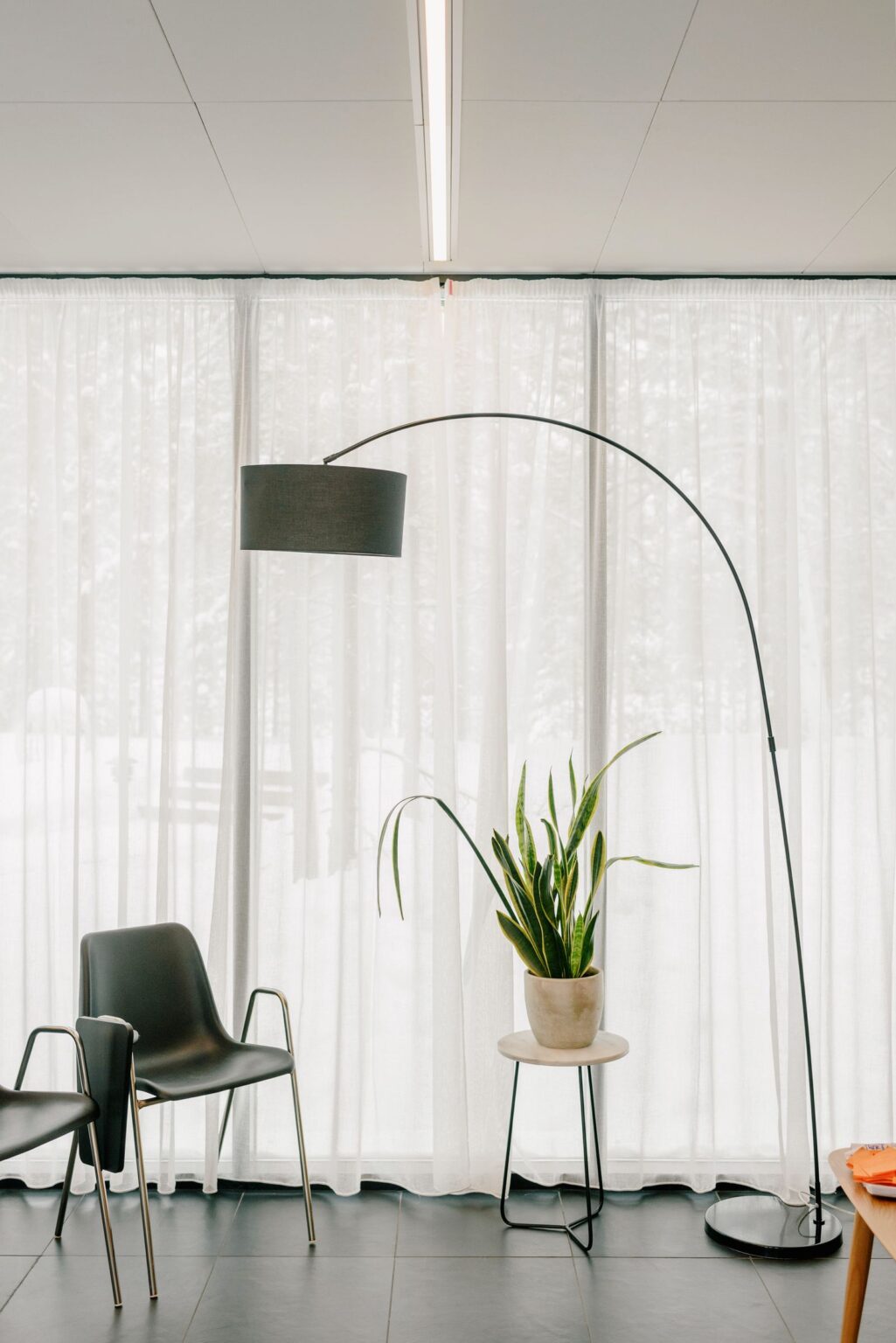 Arc floor lamp beside sheer curtains