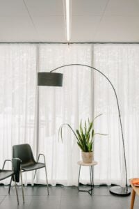 Arc floor lamp beside sheer curtains