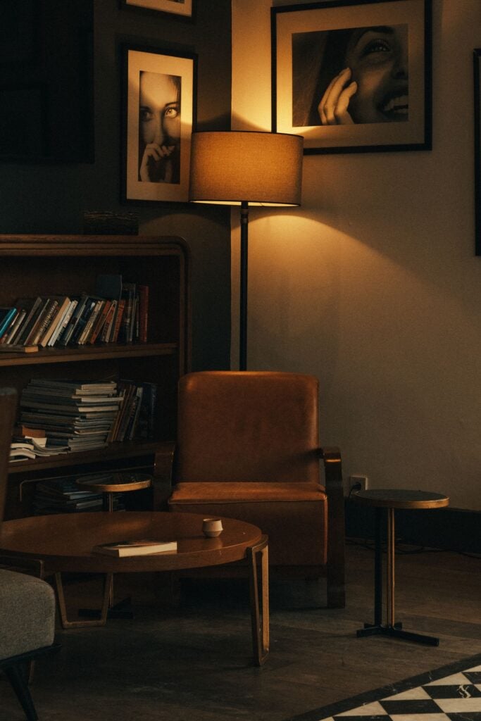 A dark study with a floor lamp glowing beside an armchair