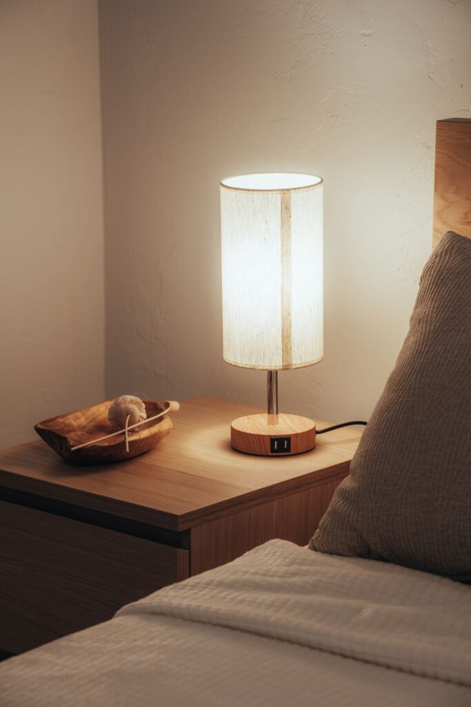 A white cylinder lamp glowing on a bedside table