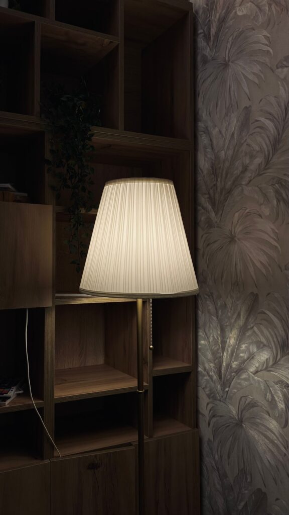Atelier Floor Lamp with a tall pleated shade by dark oak shelves