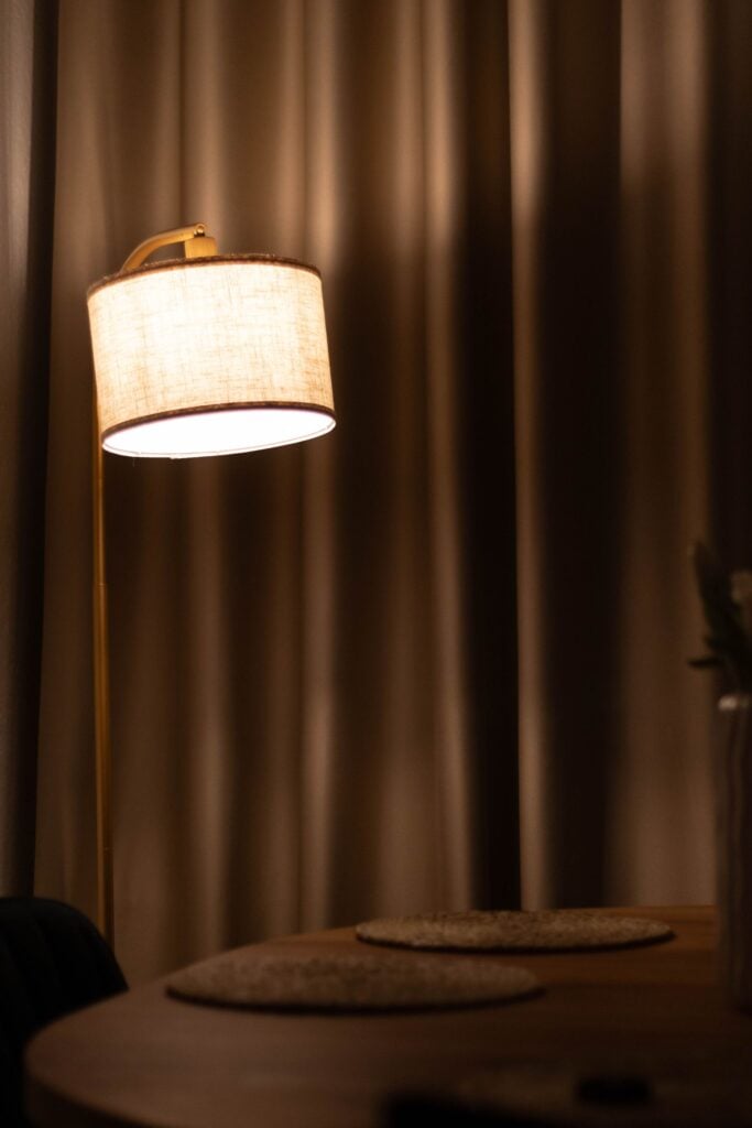 A linen floor lamp beside a curtain
