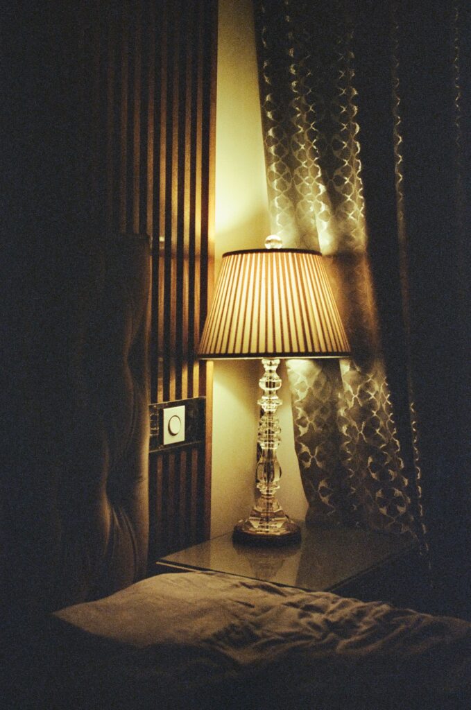 A pleated table lamp glowing by a curtain at night