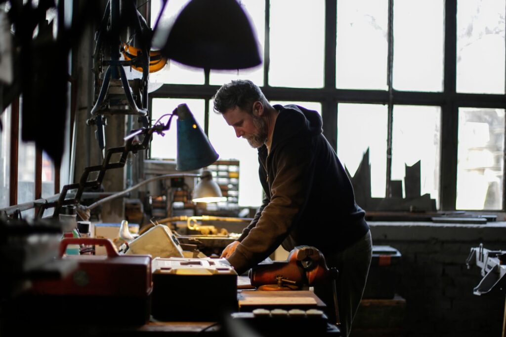 A craftsman working at a long bench under a tall workshop window