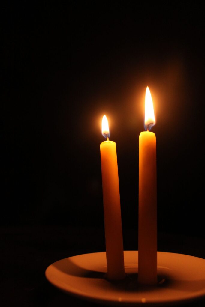 Two tapered candles burning in the dark