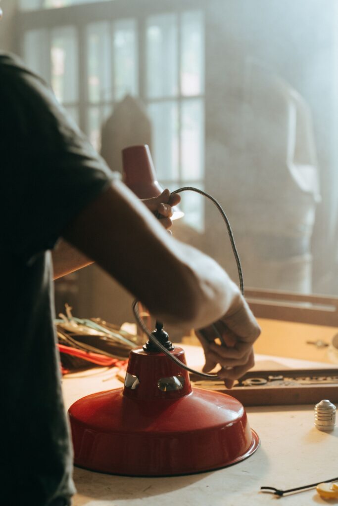 Hands threading a braided cord through a red lamp base