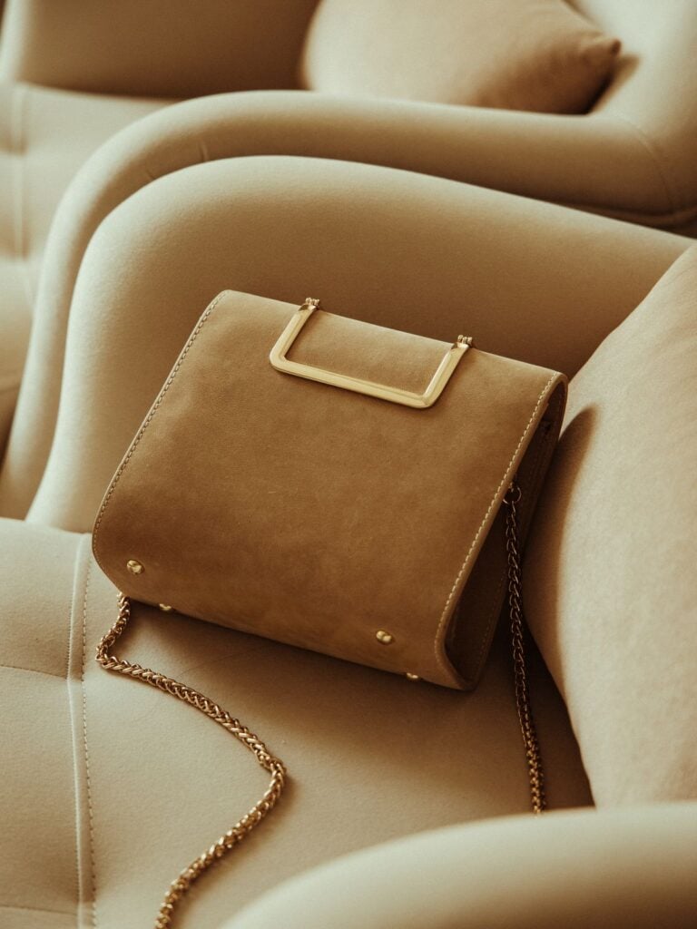 A caramel suede top handle bag resting on a cream sofa