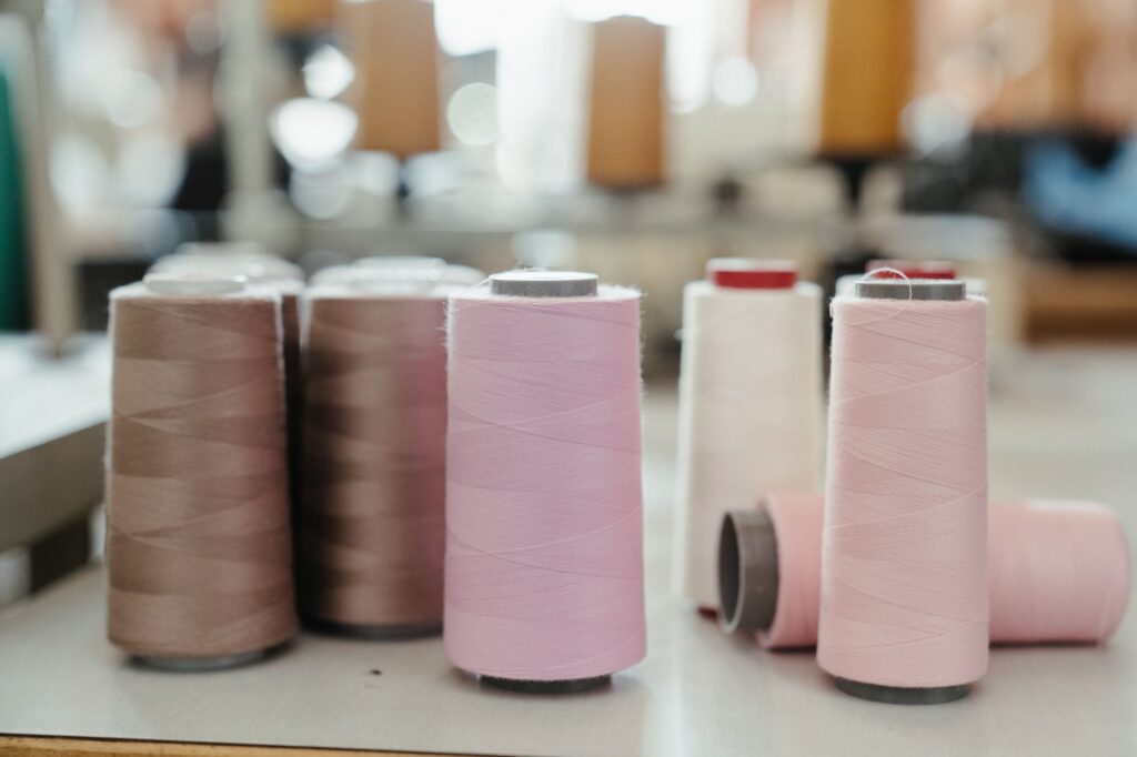 Cones of pink, mauve and white thread on a workbench