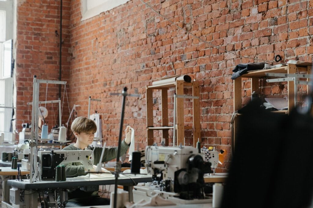 A brick walled workroom with sewing machines and a maker at work