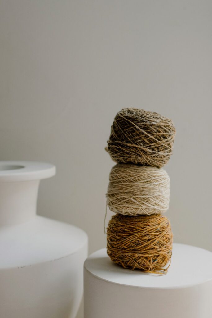 Stacked skeins of undyed wool beside a white vase