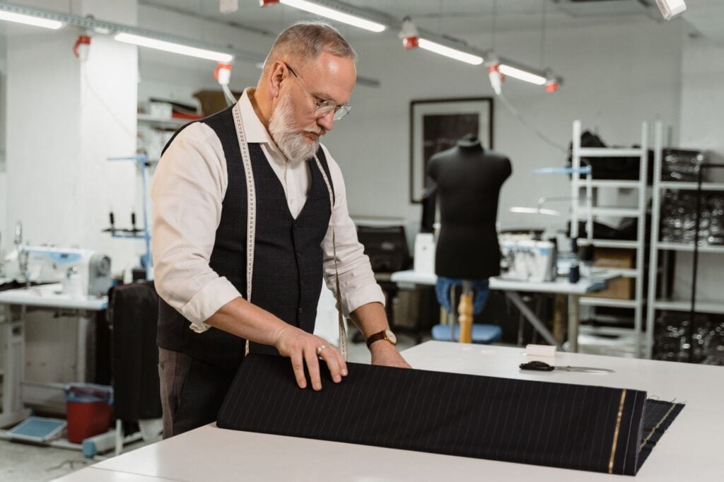 A tailor laying out dark cloth on a cutting table in the workroom