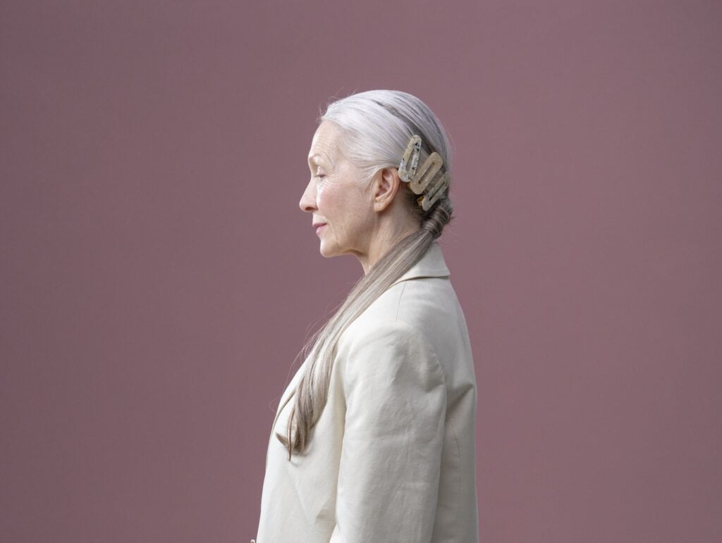 A woman in a linen blazer in profile before a wide mauve wall