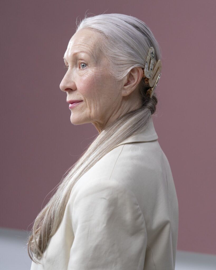 Profile of a woman with silver hair and a hair clip in a natural linen blazer against a mauve wall
