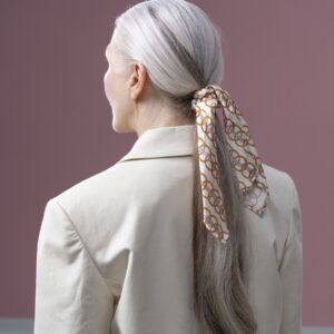 A silk scarf with a gold link print tied in long silver hair, worn with a linen blazer