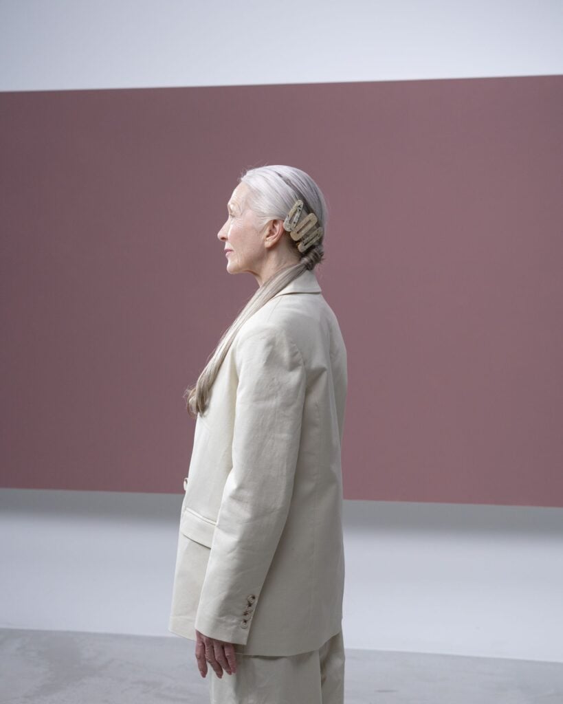 A woman in a natural linen suit standing in front of a wide mauve wall