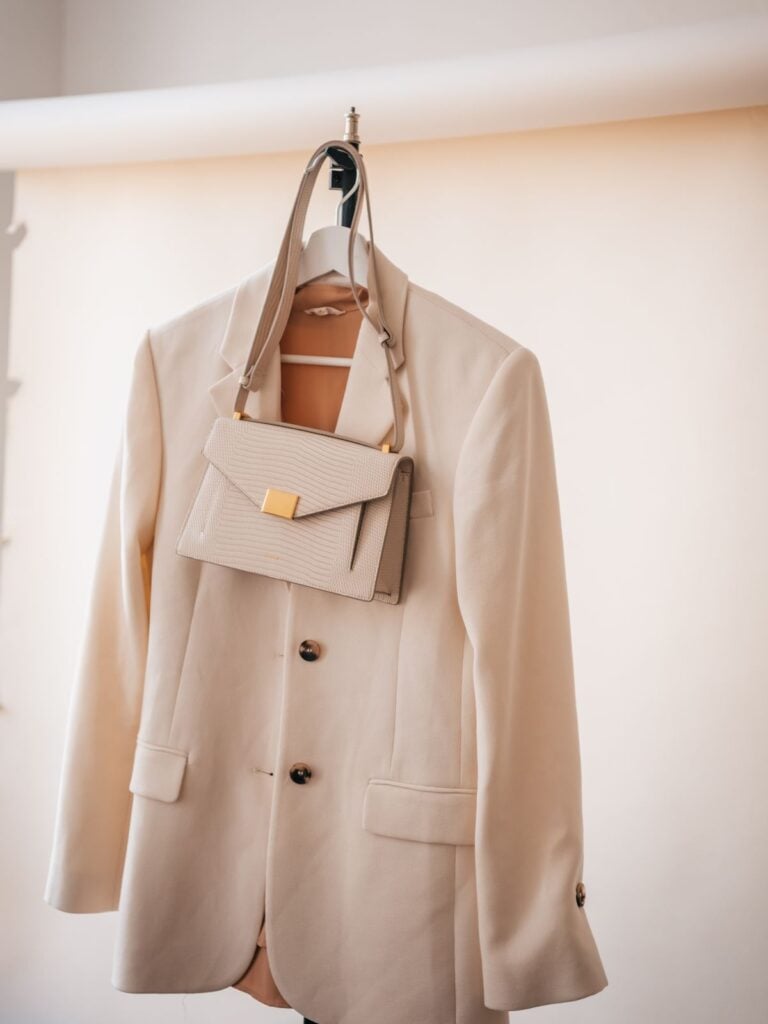 A cream blazer and a small leather bag on a hanger in soft window light